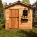 A wooden garden shed with a front door and window flower box, located in a grassy backyard, depicting the Outdoor Living Today 8×8 Gardener Shed
