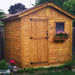 A wooden shed with a single door and a window box of pink flowers in a backyard garden, illustrating the Outdoor Living Today 8×8 Gardener Shed