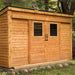 A wooden shed with double windows and doors stands under trees, showing the rustic beauty of the Outdoor Living Today GardenSaver 12×4 with Sliding Doors