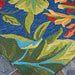 A zoomed-in corner of the Couristan Covington Indoor/Outdoor Rug - Tropical Orchid/Azure-Forest Green-Red displays bright green leaves and orange blooms against an azure background