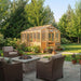 Backyard patio with chairs and a fire pit overlooks the 8x12 Outdoor Living Today Western Red Cedar Greenhouse Kit surrounded by flowers and trees