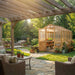 Backyard patio with seating and greenery surrounds the 8x12 Outdoor Living Today Western Red Cedar Greenhouse Kit in a landscaped yard