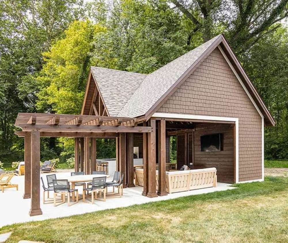 Beautifully crafted Brookside Timber Frame Denalivue Pavilion stands in a lush backyard, featuring a wooden pergola, an inviting seating area, and a covered space