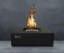 Black Warming Trends AON Steel Square Fire Pit Table is lit with bright flames against a dark gray wall background