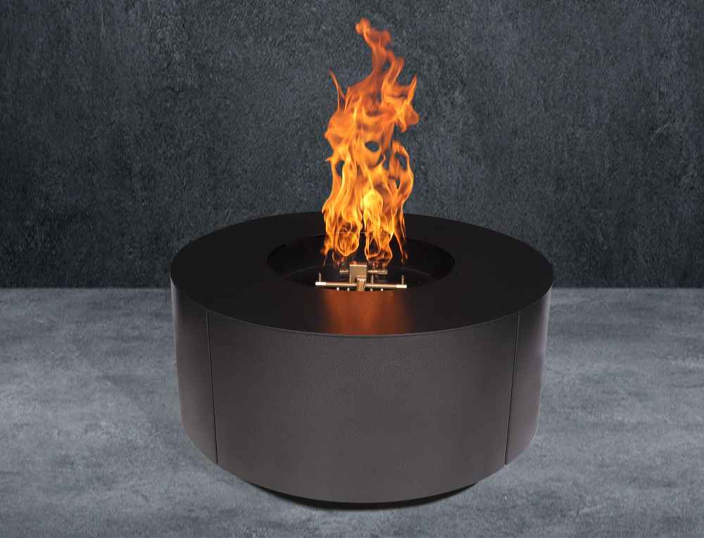 Black Warming Trends AON Steel Circular Fire Pit Table is shown burning strongly in a staged setting with a gray floor and dark wall background