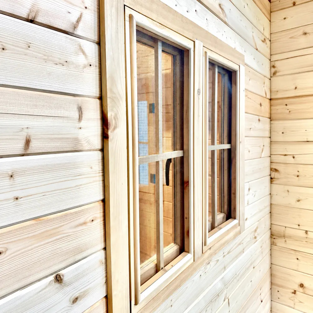 Close-up of two narrow wood-framed windows with mesh screens set into the horizontal pine siding of the BlueWater Bungalow 160.