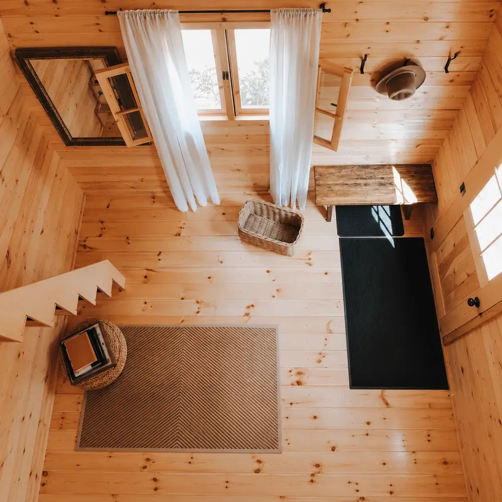 Overhead view of the BlueWater Loft 160 entry with pine flooring, black mats, a woven basket, bench, and sunlit windows.