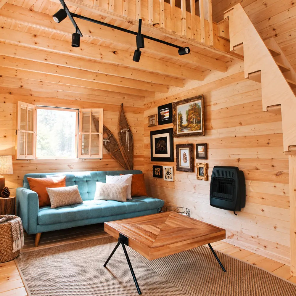 Cozy BlueWater Loft 160 living area with a teal sofa, geometric wooden coffee table, rustic wall art, and loft stairs.