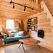 Cozy BlueWater Loft 160 living area with a teal sofa, geometric wooden coffee table, rustic wall art, and loft stairs.