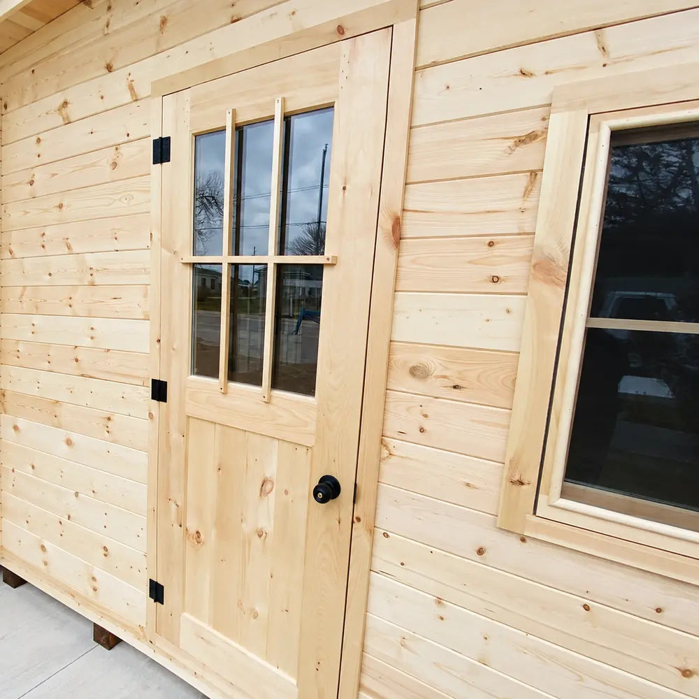 Close-up of the Bluewater Den 67 wooden door and adjacent window highlighting the pale wood grain and sturdy black hardware.