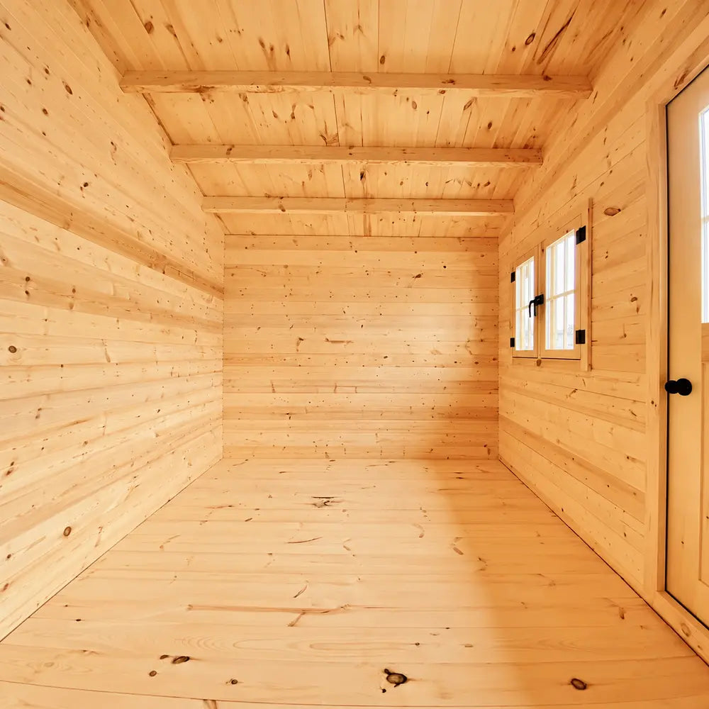 Empty Bluewater Den 67 interior with smooth pine flooring, exposed ceiling beams, a double window and a partially visible wooden door.