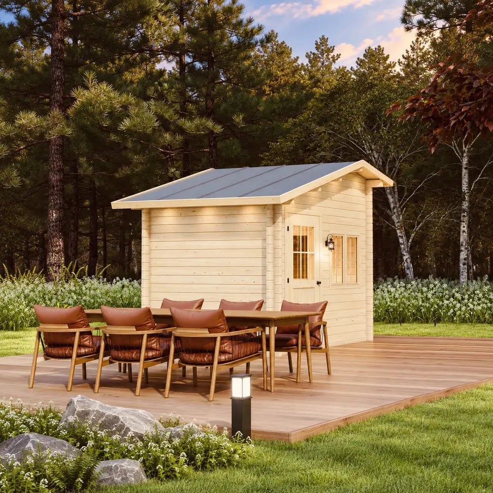 Rear-corner view of the Bluewater Den 67 behind a large outdoor dining table with brown cushioned chairs on a wooden deck.