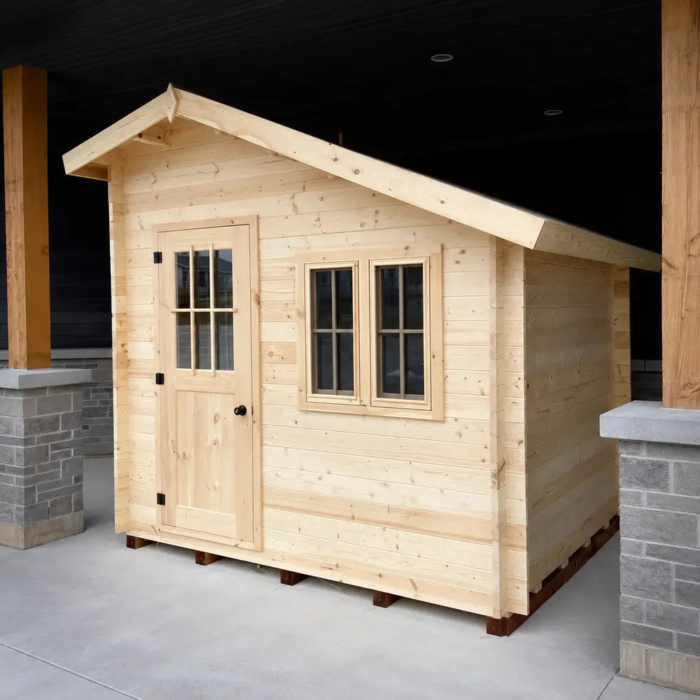 Right-angled view of the Bluewater Den 67 highlighting its pale wood siding, black door hardware, front windows and extended sloped roof.