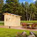 Side-angle view of the Bluewater Den 67 with its sloped roof, wooden deck and outdoor dining area surrounded by trees and flowers.