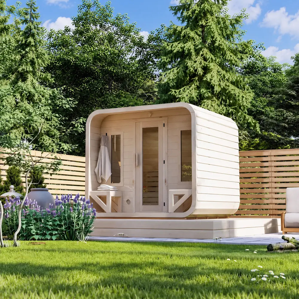Side-angle view of the Sawmill Structures Box Sauna surrounded by green trees, purple flowers, lawn, and a horizontal wooden privacy fence.