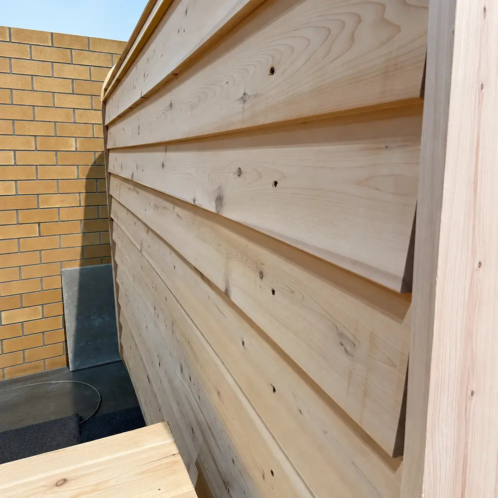 Close side view of the Sawmill Structures Box Sauna highlighting its overlapping pale wooden exterior panels, natural grain, and weather-resistant construction.