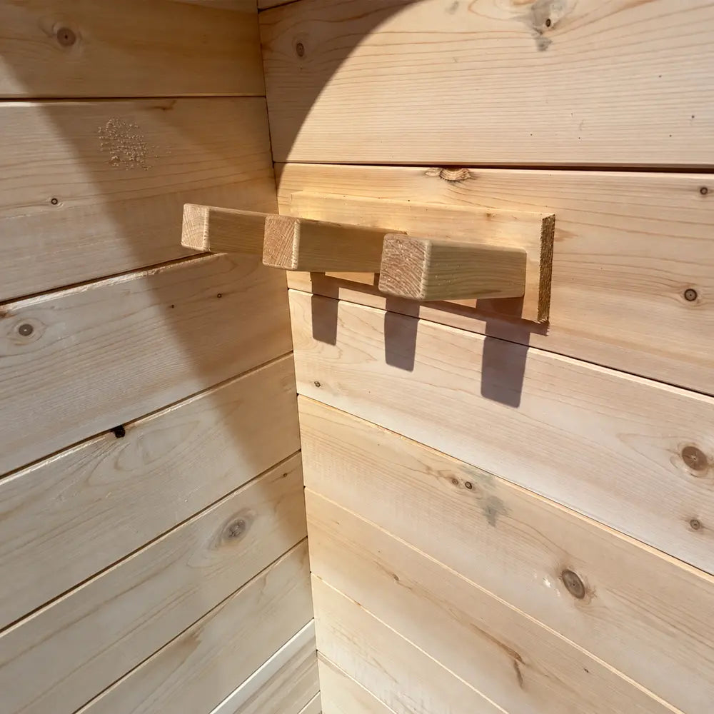 Close-up of three sturdy wooden hooks mounted on the pale horizontal wall paneling inside the Sawmill Structures Box Sauna.