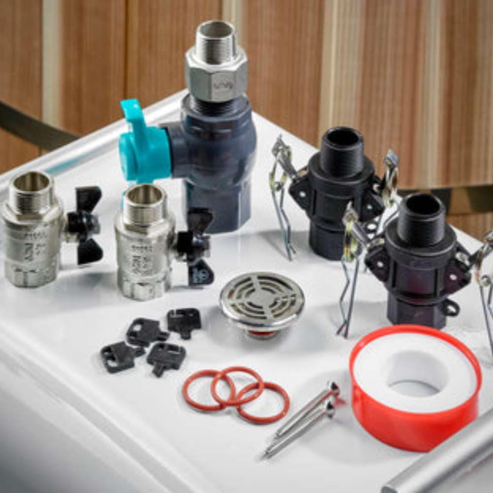 Brass and gray ball valves, black hose connectors, a drain grate, red O-rings and white thread seal tape for Golden Designs Dynamic Cold Therapy Oval Barrel Pacific Cedar Cold Plunge are laid out on a white tub edge