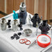Brass and gray valves, black hose connectors, a drain grate, red O-rings and thread seal tape for Golden Designs Dynamic Cold Therapy Cuboid 304 Nano-Coated Stainless Steel Cold Plunge Tub XL lie on a white surface