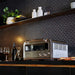 Breville® Smart Oven® Pizzaiolo Pizza Oven sits on a dark kitchen counter beside pizza, wine glasses, and bottles