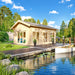 Britt 44 wooden garden room beside a landscaped pond, with expansive glass doors, a furnished deck and outdoor dining area.