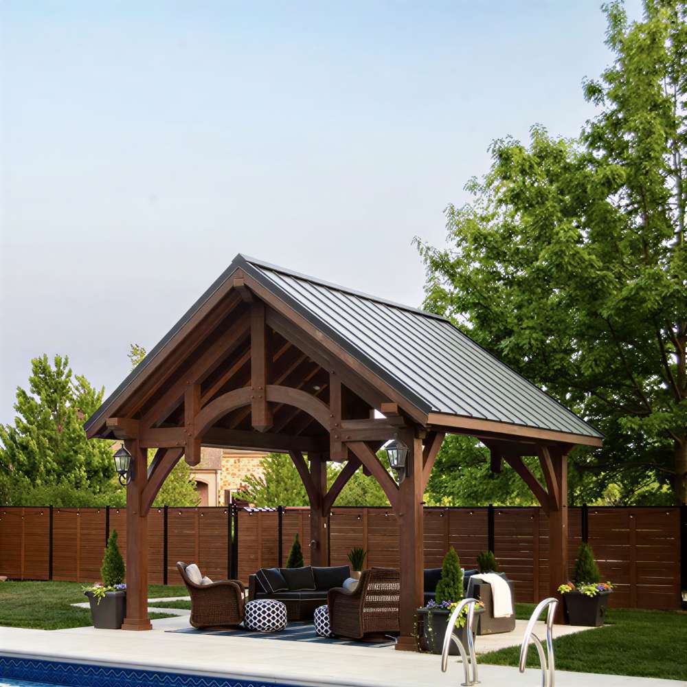 Brookside Timber Frame Alpine Lodge Pavilion is a poolside wooden pavilion with a sloped roof shading a comfortable outdoor seating space