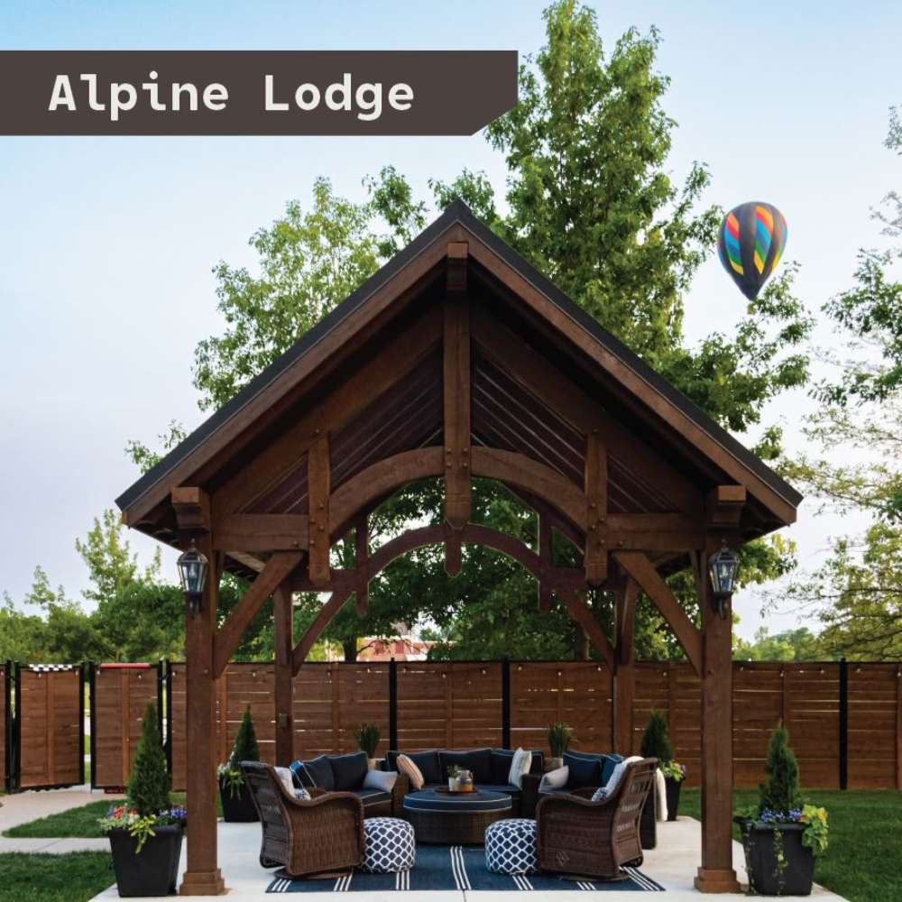 Brookside Timber Frame Alpine Lodge Pavilion is a wooden outdoor shelter with a high gabled roof covering a cozy seating area in a fenced backyard