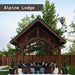 Brookside Timber Frame Alpine Lodge Pavilion is a wooden outdoor shelter with a high gabled roof covering a cozy seating area in a fenced backyard