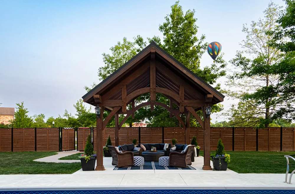 Brookside Timber Frame Alpine Lodge Pavilion is perfectly positioned by a pool, with a hot air balloon in the background
