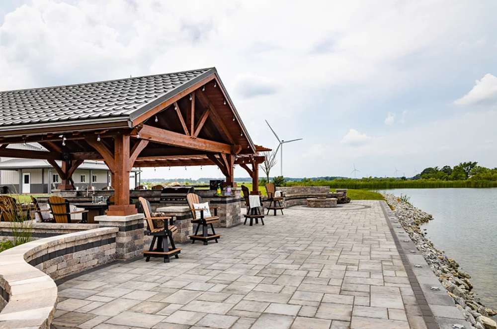 Brookside Timber Frame Combolan Estate Pavilion offers a relaxing waterfront retreat with ample seating, a covered roof, and a breathtaking landscape view