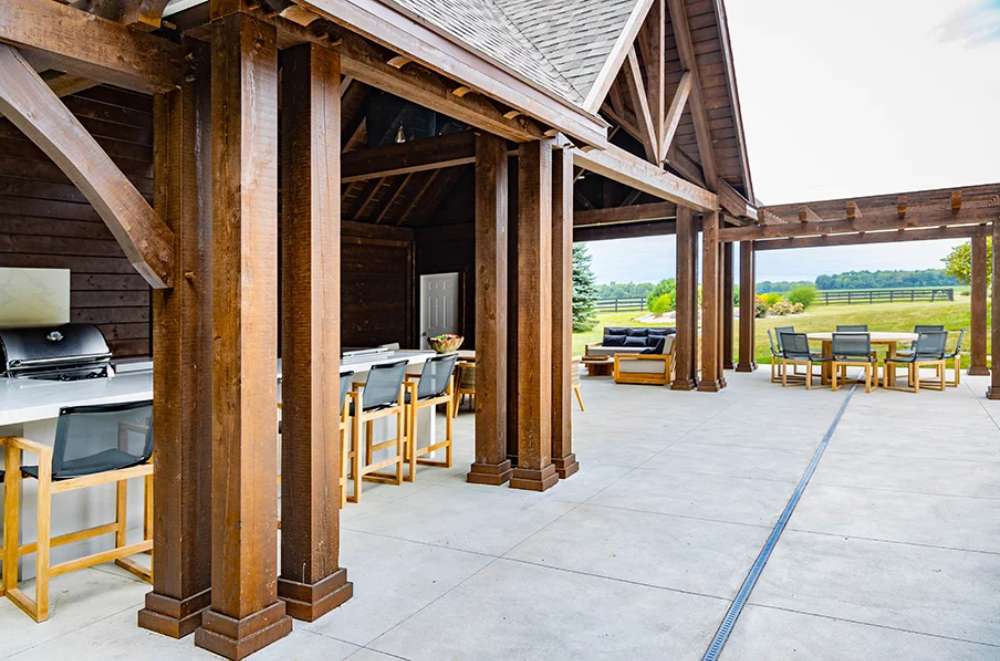 Brookside Timber Frame Denalivue Pavilion showcases a spacious outdoor kitchen and bar area, with sturdy wooden beams, sleek countertops, and modern seating