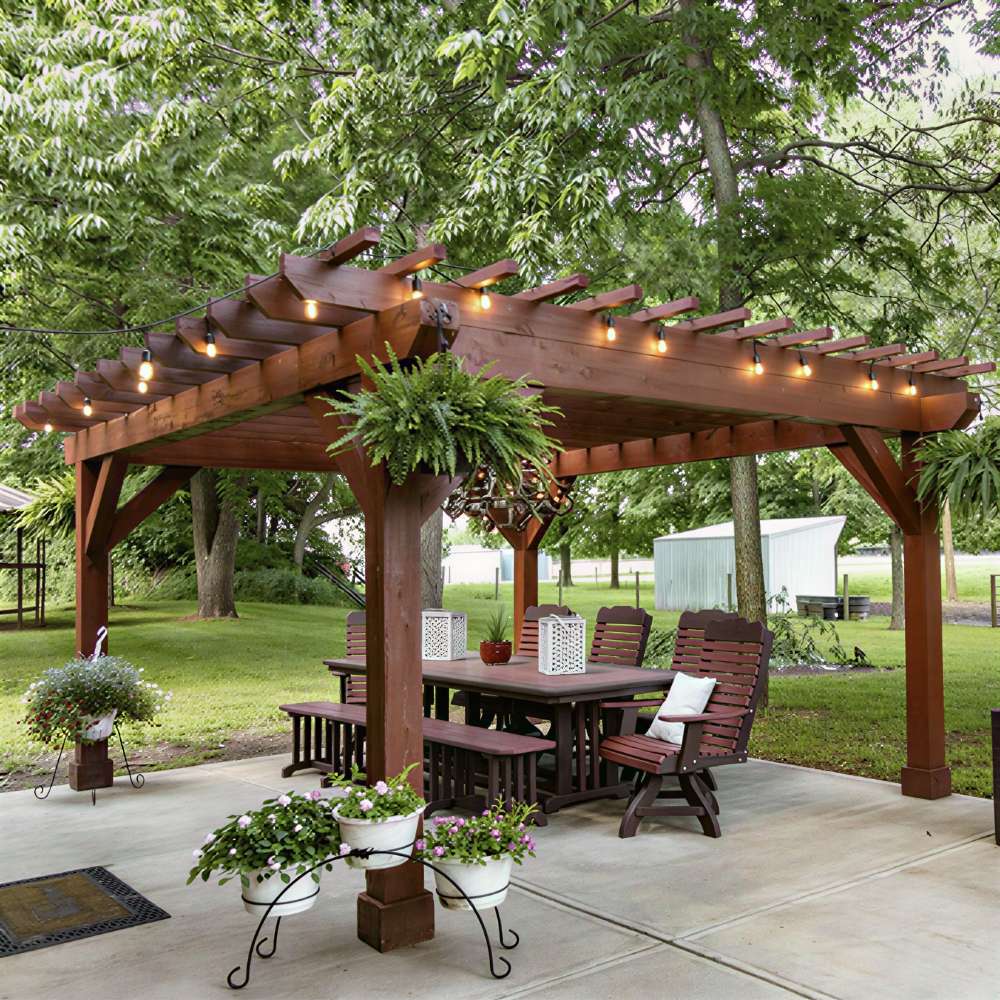 Brookside Timber Frame Fern Shade Pergola stands prominently over a patio table, with hanging plants and soft lighting set against a leafy backyard