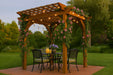 Brookside Timber Frame Hawthorne Pergola shades a backyard dining set with four chairs, climbing flowers, and warm string lighting