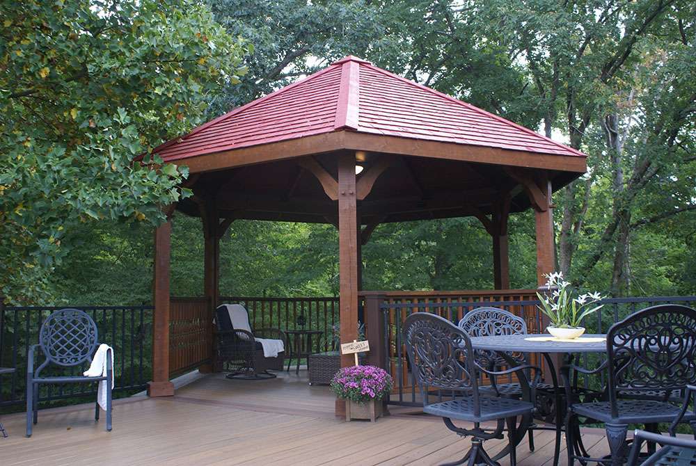 Brookside Timber Frame Lakeside Majestic Pavilion on a deck with outdoor furniture in a peaceful forest setting