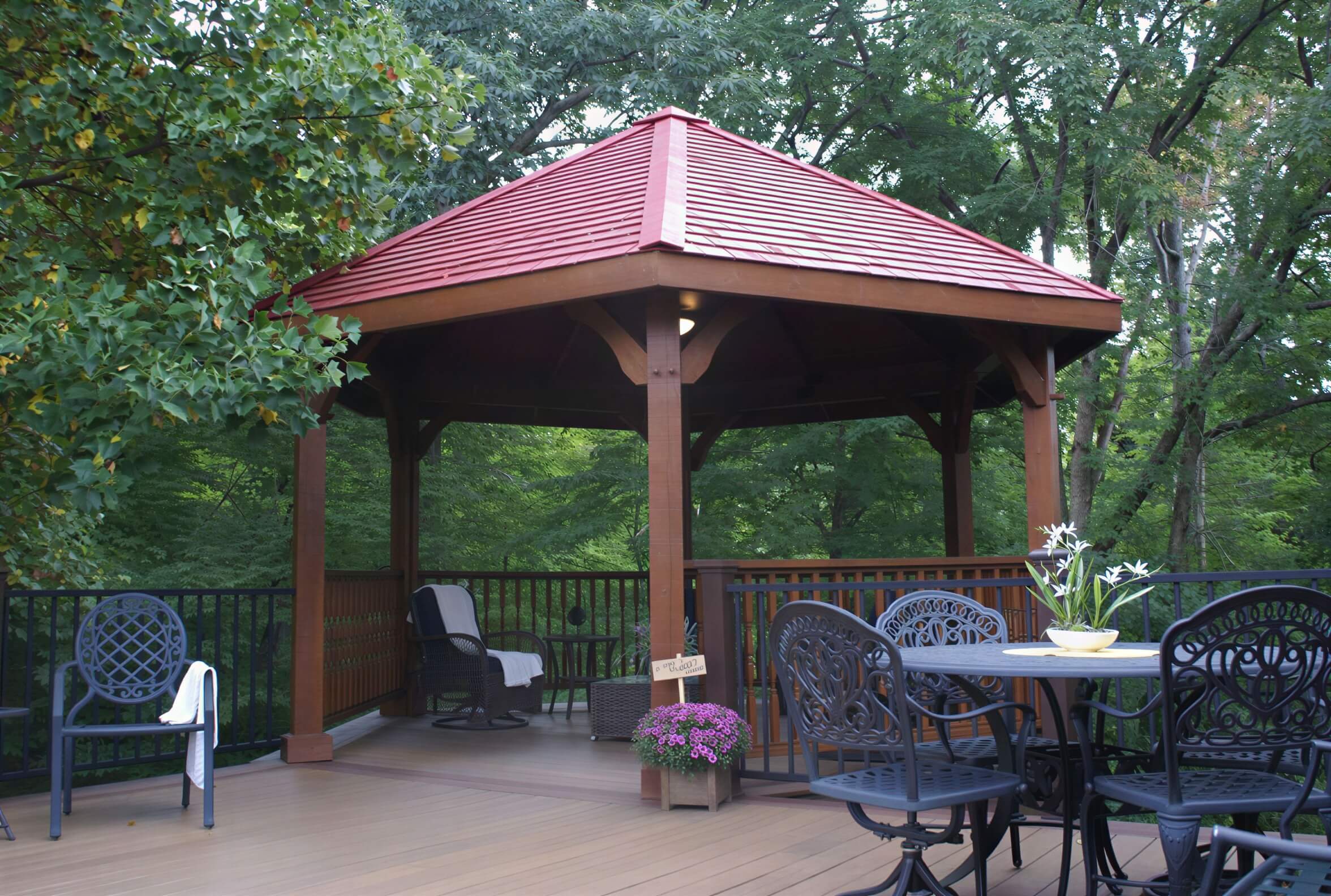 Brookside Timber Frame Lakeside Majestic Pavilion on a deck with outdoor furniture in a peaceful forest setting