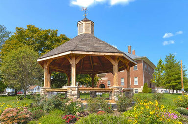 Brookside Timber Frame Lakeside Majestic Pavilion on a sunny day with a detailed roof and blooming garden around it