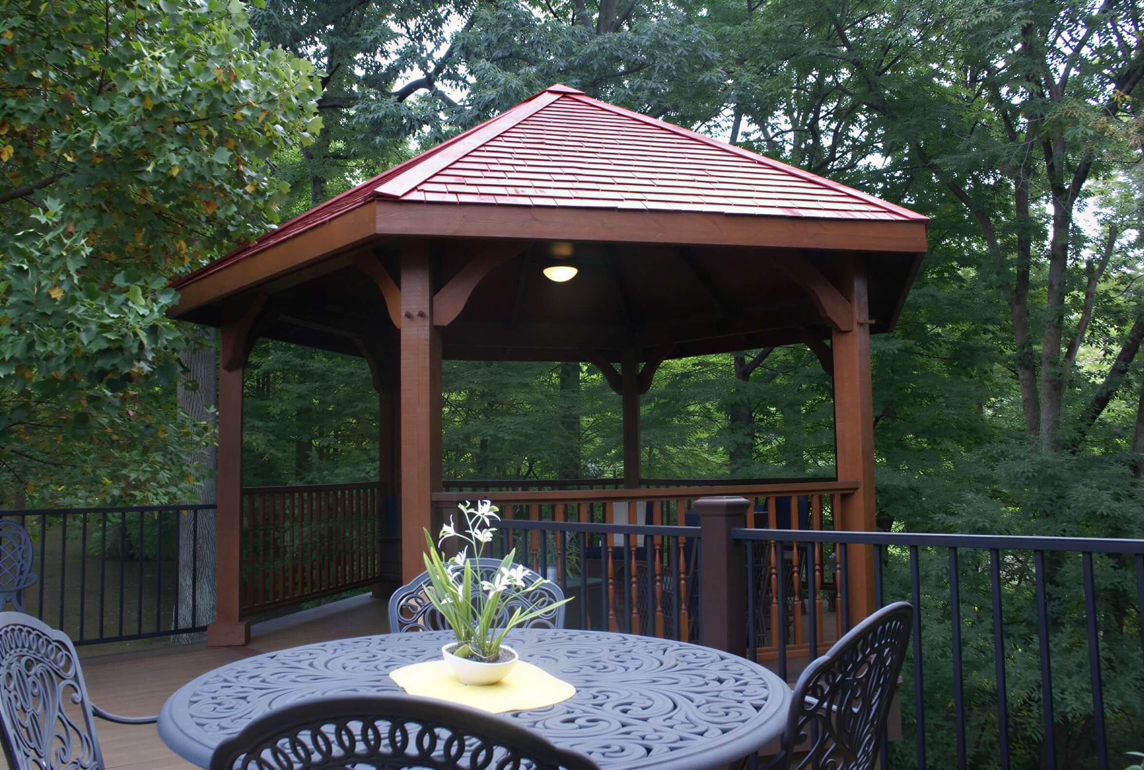 Brookside Timber Frame Lakeside Majestic Pavilion on a wooded deck with a red roof and cozy seating underneath