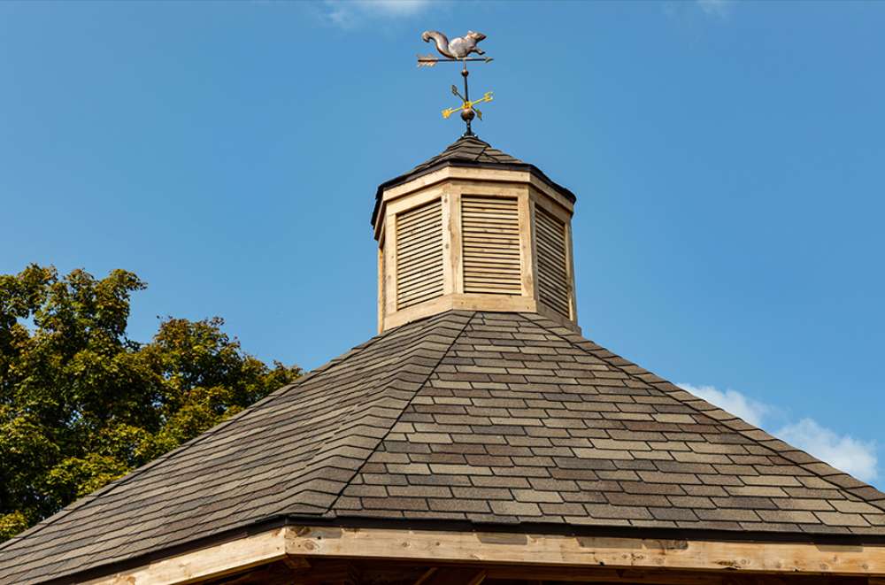 Brookside Timber Frame Lakeside Majestic Pavilion roof peak with cupola and weather vane against blue sky