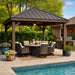 Brookside Timber Frame Stonewood Pavilion is beside a swimming pool with a shaded dining set underneath, surrounded by greenery and a nearby outdoor kitchen