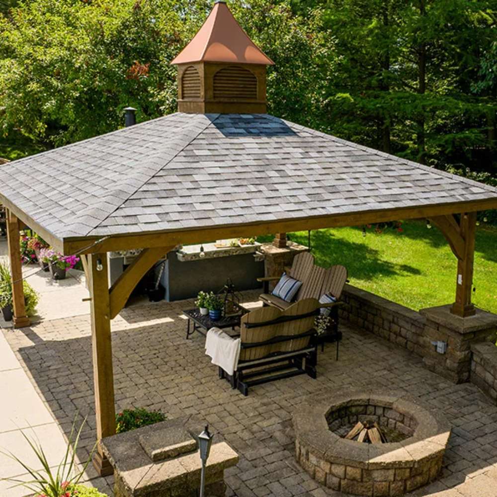 Brookside Timber Frame Forest Melody Pavilion creates a perfect entertainment space with comfortable seating, a fire pit, and an outdoor kitchen