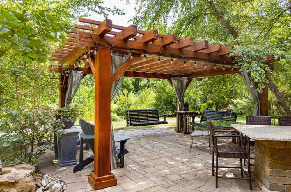 Brookside Timber Frame Highlan Oasis Pergola is a beautifully crafted wooden pergola set in a lush backyard