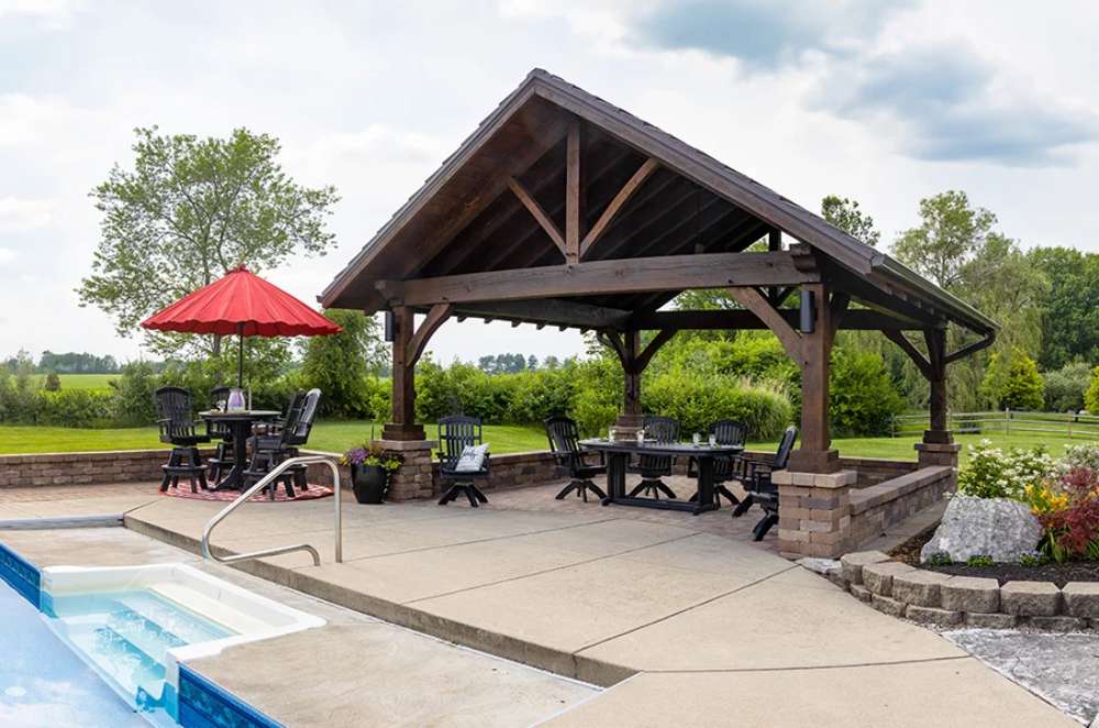 Brookside Timber Frame Timber Retreat Pavilion provides a luxurious poolside shelter, surrounded by lush greenery and featuring a stylish outdoor seating area