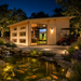 Caddie 44A ALU ISO illuminated golf simulator room at night with a parked golf cart, landscaped koi pond, visible koi fish, and pathway lighting.