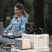 Camper uses a laptop while Jackery Explorer 300D Portable Power Station powers devices on a campsite table