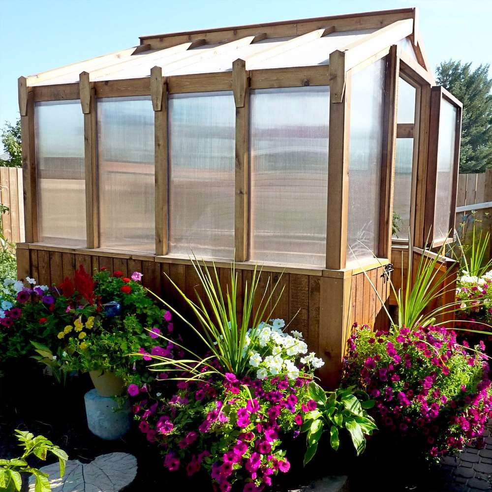 Cedar greenhouse surrounded by bright flowers showcases the 8x8 Outdoor Living Today Western Red Cedar Greenhouse Kit in a garden setting