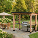 Cedar wood grill shelter on a stone patio beside outdoor dining furniture, the Outdoor Living Today Western Red Cedar 8x5 Grill Gazebo creates a shaded cooking space in a green backyard