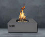 Charcoal Warming Trends AON Steel Square Fire Pit Table is shown with flames rising high against a dark wall backdrop