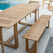 Close angled outdoor view focuses on the bench and table of Westminster Teak Horizon Table & Bench Set placed on a patio near a pool