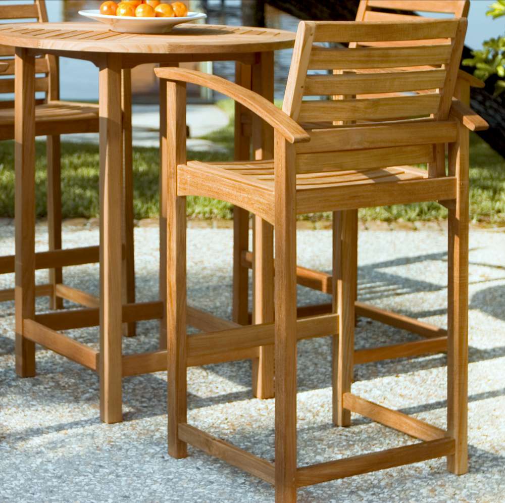 Close outdoor view shows Westminster Teak Somerset Teak Bar Stool next to a round table with a bowl of oranges, set on a patio with water in the background