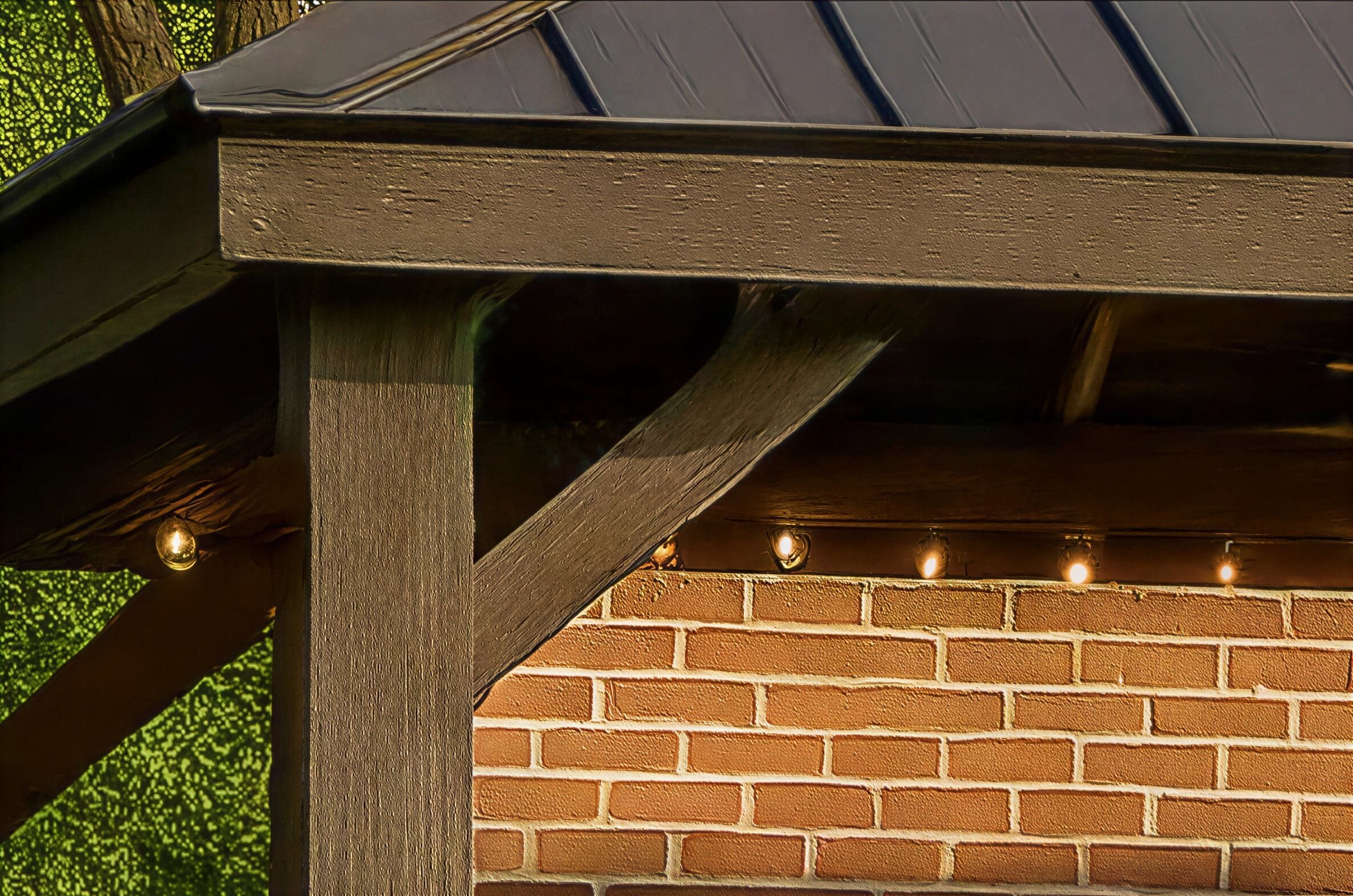 Close-up of Brookside Timber Frame Stonewood Pavilion highlights its sturdy wooden post, angled support beams, and string lights beneath the roof